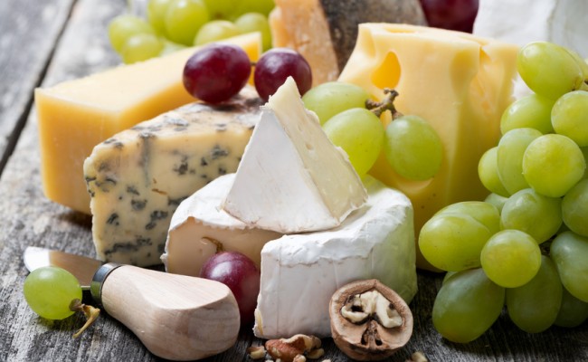 assortment of fresh cheeses and grapes on a wooden background